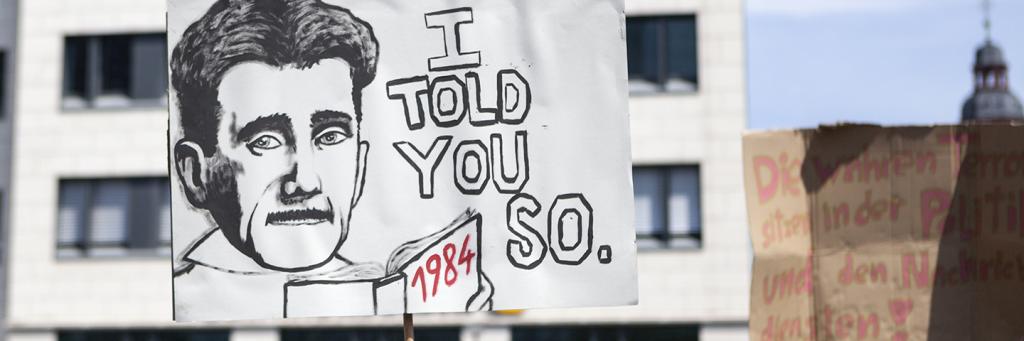 Man holds poster saying I told you so, with 1984 written at the bottom, the book by George Orwell