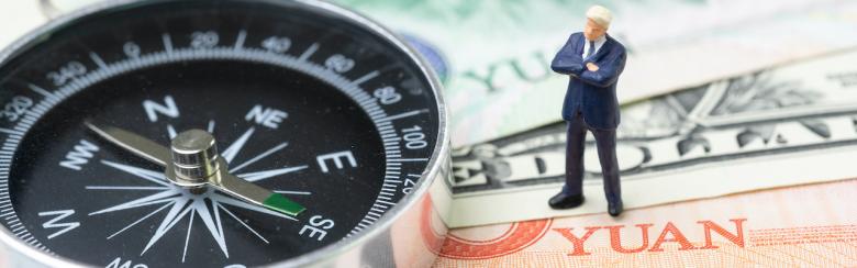 Compass with miniature leader standing on US dollar and China yuan banknotes.